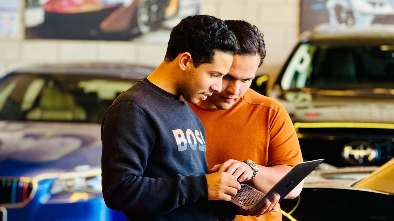 Dois integrantes da equipe da DUO MOTORS conferindo dados de um carro no notebook